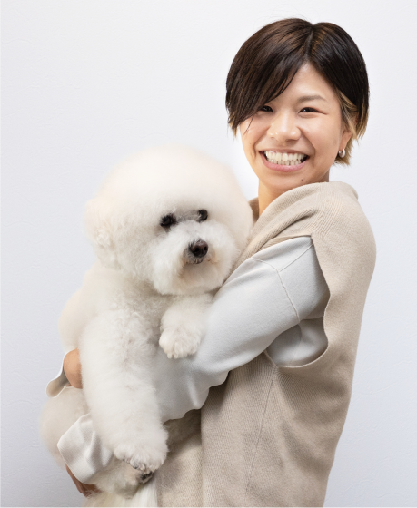 写真：笑顔で犬を抱っこするトリミングサロンオーナー